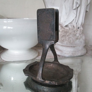 May include: A vintage metal ashtray with a unique design. The ashtray has a rectangular top with a small opening and a triangular base with a circular dish.