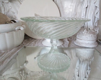 May include: A clear glass pedestal bowl with a swirl design. The bowl is empty and sits on a white surface.