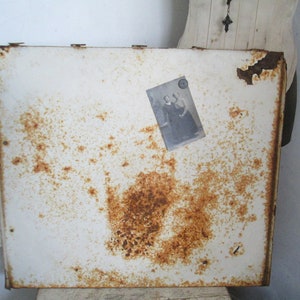 May include: White metal cabinet door with rust spots and a black and white photo of two people in vintage clothing attached to the door.