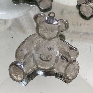 May include: Silver teddy bear charm with a loop for hanging. The charm has a detailed design and the inscription "REINZINK 925" on the bottom.