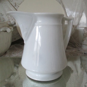 May include: A white porcelain jug with a flared spout and a handle. The jug has a smooth, glossy finish.