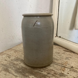 Puede incluir: Un tarro de cerámica blanco con una superficie ligeramente texturizada. El tarro tiene un cuerpo redondeado y una boca ancha.