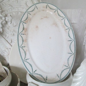 May include: A white oval serving platter with a green floral design around the edge. The platter is slightly worn and has a rustic look.