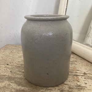 Può includere: Un vaso di ceramica grigio con una superficie liscia e leggermente ruvida. Il vaso ha un corpo arrotondato e una bocca larga.