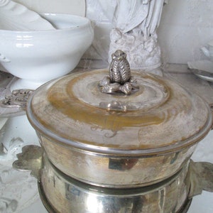 Può includere: Un piatto da portata in argento con un coperchio e un motivo floreale decorativo sulla parte superiore. Il piatto è rotondo e ha una finitura lucida.