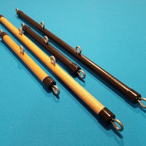 May include: Four wooden and black pool cue racks with metal ring attachments. Two are light wood with black tips, and two are black with black tips. The racks are arranged diagonally on a blue surface.
