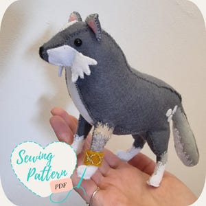 May include: A gray and white plush wolf sewing pattern. The wolf has a white muzzle and a gold band around its leg. The pattern is available as a PDF download.
