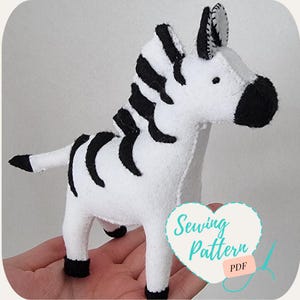 May include: A white and black felt zebra sewing pattern. The pattern is in the shape of a zebra with black stripes and a black nose. The pattern is on a white background and has the words "Sewing Pattern PDF" on it.