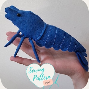 May include: A blue felt sewing pattern for a shrimp. The pattern is in the shape of a heart and says "Sewing Pattern PDF" on it.