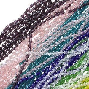 Puede incluir: Hilos de cuentas de vidrio facetadas en varios colores, incluyendo morado, rosa, turquesa, azul y verde. Las cuentas, de forma ovalada, están ensartadas, creando un efecto brillante. Ideal para la creación de joyas y proyectos de artesanía.