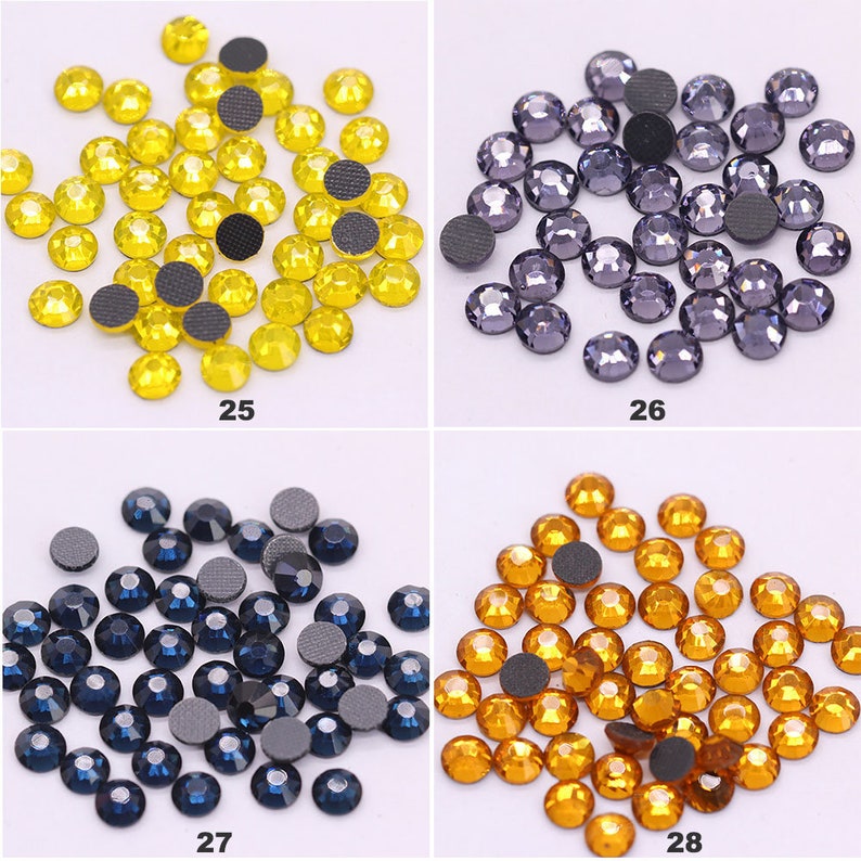 May include: Assortment of four colors of rhinestones, each color in a separate pile. The colors are yellow, purple, blue, and orange. Each rhinestone has a flat back with a black adhesive.