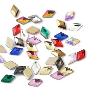 May include: Assortment of colorful diamond-shaped rhinestones in various colors, including red, green, blue, gold, and clear. The rhinestones are scattered on a white background.