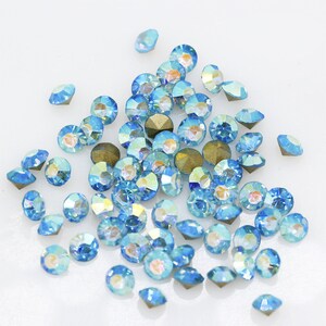 Pu&ograve; includere: Un grande gruppo di strass blu chiaro iridescenti, sparsi su una superficie bianca.