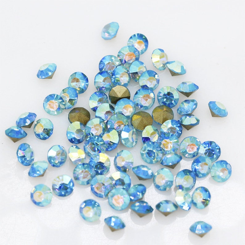Pu&ograve; includere: Un grande gruppo di strass blu chiaro iridescenti, sparsi su una superficie bianca.