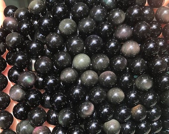 May include: A close-up of a pile of black obsidian beads with iridescent shimmer. The beads are round and smooth, and they are perfect for making jewelry.