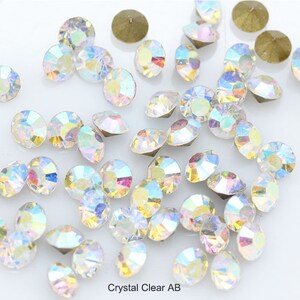Pu&ograve; includere: Una grande quantit&agrave; di strass AB trasparenti iridescenti, sparsi su una superficie bianca. Gli strass sono di varie dimensioni e forme, con un effetto arcobaleno.