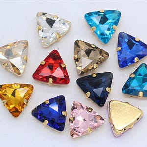 May include: Assortment of triangle-shaped rhinestones in various colours, including clear, gold, red, blue, pink, and turquoise. The rhinestones have a gold-toned metal setting.