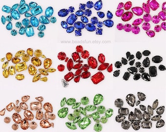 May include: Assortment of colorful glass rhinestones in various shapes and sizes. The rhinestones are arranged in rows on a white background. The rhinestones are perfect for crafting, jewelry making, and decorating.