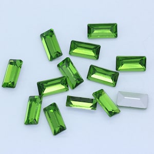 May include: A scattering of green rectangular rhinestones on a white background.