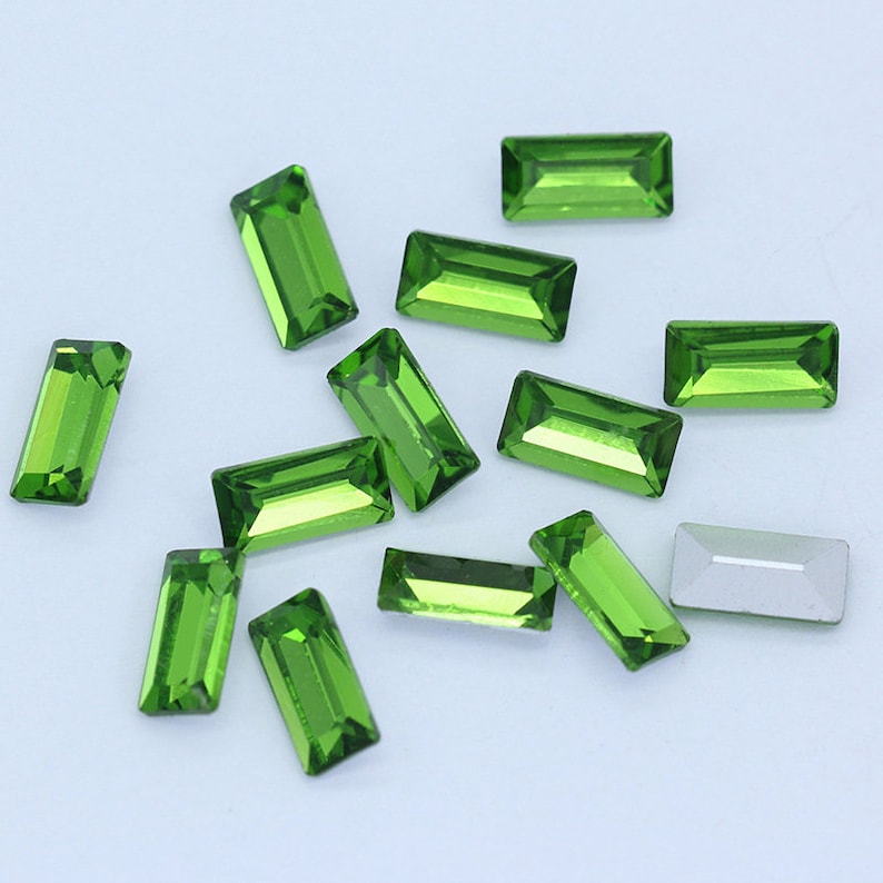May include: A scattering of green rectangular rhinestones on a white background.