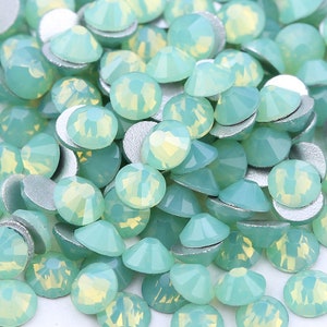 Könnte beinhalten: Ein großer Haufen hellgrüner, facettierter, runder Glas-Straßsteine. Die Strasssteine haben eine silberne Rückseite.