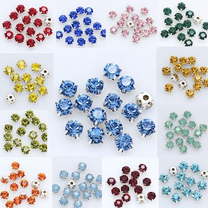 May include: A selection of colourful rhinestone embellishments in shades of red, blue, pink, green, yellow, and orange. Each rhinestone has a faceted design and is set in a silver-tone metal base. Suitable for crafting and jewellery making.