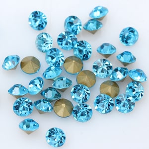 May include: A scattering of turquoise blue rhinestones with gold settings. The rhinestones are round and have a faceted design.