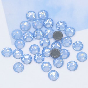 Puede incluir: Una dispersión de piedras de cristal azul claro iridiscentes sobre un fondo blanco.