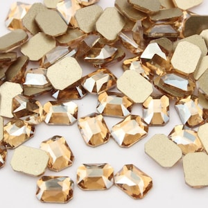 Puede incluir: Una gran cantidad de pequeños diamantes de imitación de vidrio rectangulares transparentes con un ligero color ámbar. Los diamantes de imitación están esparcidos sobre una superficie blanca.