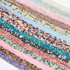 May include: A collection of beaded strands in various colors, including pink, blue, green, and purple. The beads appear to be small and faceted, creating a sparkling effect. The strands are arranged diagonally, showcasing the variety of colors and textures.