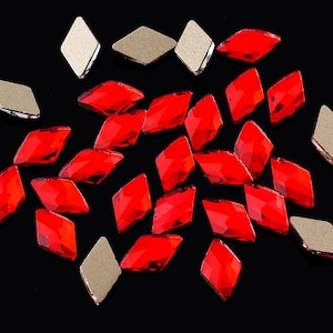 May include: A group of red diamond-shaped rhinestones on a black background. The rhinestones are scattered in a random pattern.