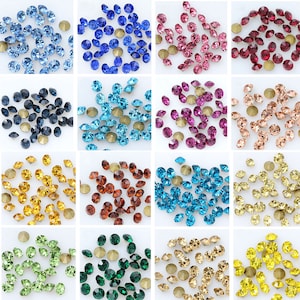 May include: Assortment of 12 colors of round glass rhinestones, each color displayed in a separate pile on a white background.