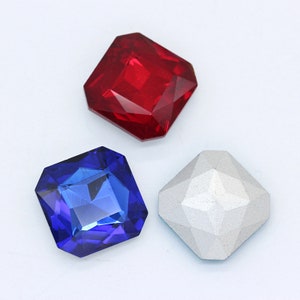 May include: Three square-shaped rhinestones. One is red, one is blue, and one is silver.