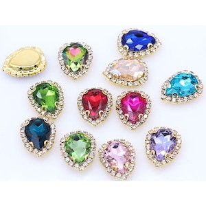 May include: Assortment of 12 teardrop-shaped rhinestones with gold settings and clear crystal accents. The rhinestones are in various colors, including red, green, blue, pink, and purple.