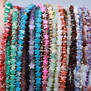 Puede incluir: Una colección de hilos de cuentas con cuentas en forma de estrella en varios colores, incluyendo rojo, turquesa, rosa y blanco. Las cuentas están ensartadas, creando una exhibición colorida y texturizada. Ideal para la fabricación de joyas o proyectos de artesanía.