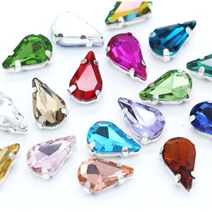 May include: Assortment of teardrop-shaped rhinestones in various colours, including clear, red, green, blue, purple, pink, and brown. The rhinestones have a silver setting.