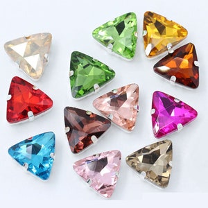 May include: Assortment of twelve triangle-shaped rhinestones with silver settings. The rhinestones are in various colors, including red, green, blue, pink, brown, and clear.