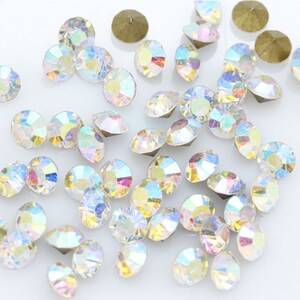 Pu&ograve; includere: Una grande quantit&agrave; di strass di vetro trasparente iridescente, noti anche come cristalli, di varie dimensioni. Gli strass sono sparsi su una superficie bianca.