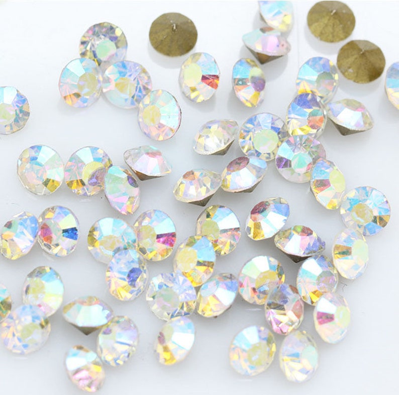 Pu&ograve; includere: Una grande quantit&agrave; di strass di vetro trasparente iridescente, noti anche come cristalli, di varie dimensioni. Gli strass sono sparsi su una superficie bianca.