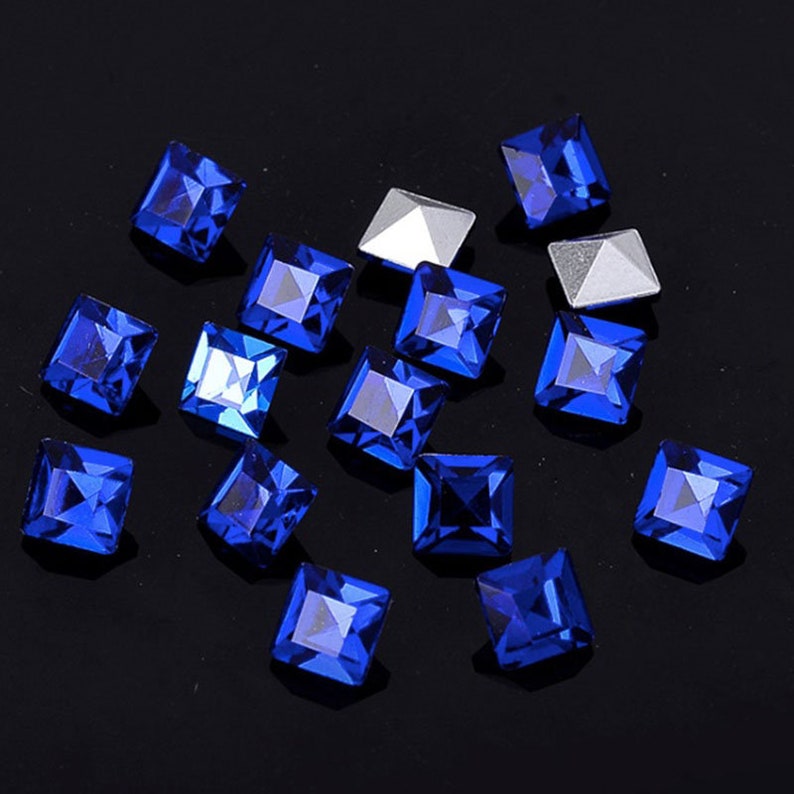 May include: A scattering of small, square, blue rhinestones on a black background.