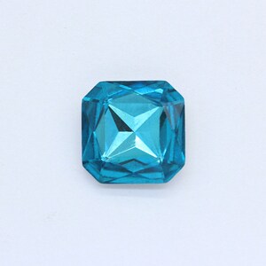May include: A single, large, faceted, turquoise blue gemstone. The gemstone is square shaped with rounded edges.