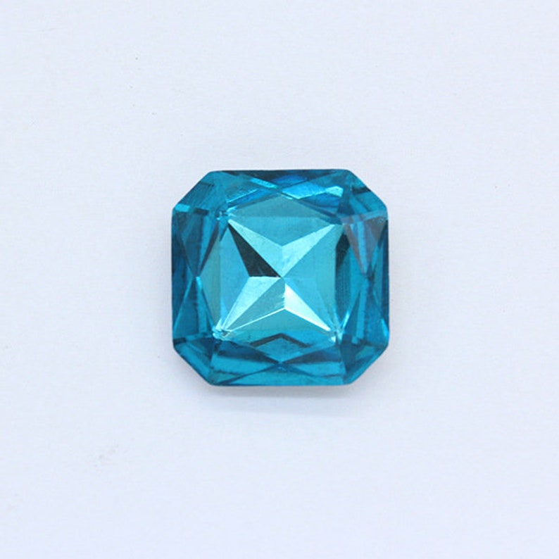 May include: A single, large, faceted, turquoise blue gemstone. The gemstone is square shaped with rounded edges.