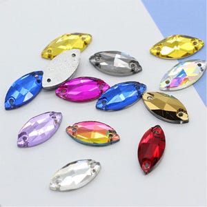 Può includere: Assortimento di strass ovali sfaccettati di vari colori. Gli strass sono di vari colori, tra cui blu, viola, rosso, oro, argento e trasparente.