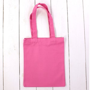 May include: A pink tote bag with two handles. The bag is made of a soft, cotton fabric.