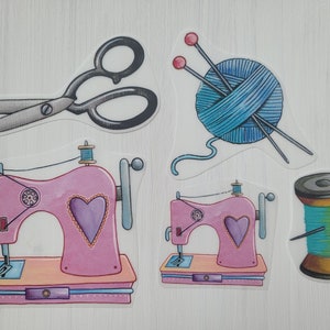 Könnte beinhalten: Ein Set mit fünf bunten Stickerei-Aufklebern. Die Aufkleber beinhalten eine Schere, eine Garnrolle, eine Wollknäuel mit zwei Nadeln und zwei rosa Nähmaschinen mit Herzen.