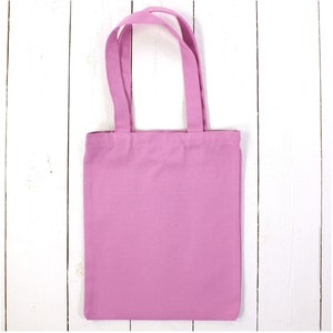 May include: A plain pink tote bag with fabric handles. The bag is made of a soft, cotton material.