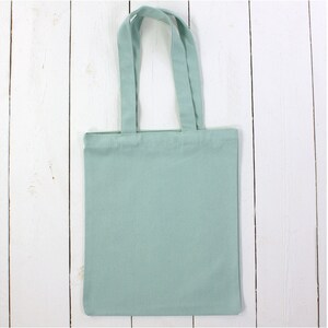 May include: A light green tote bag with two handles. The bag is made of canvas and has a plain design.