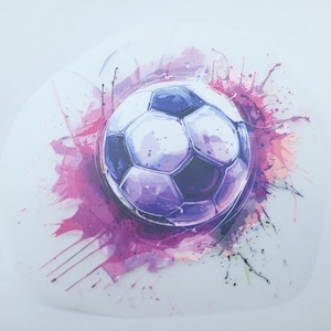 Könnte beinhalten: Ein weißer und lilafarbener Fußball mit einem rosafarbenen Aquarell-Spritzeffekt drumherum.