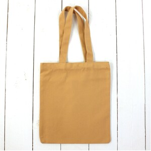 May include: A plain, light brown tote bag with two handles. The bag is made of canvas and has a simple design.