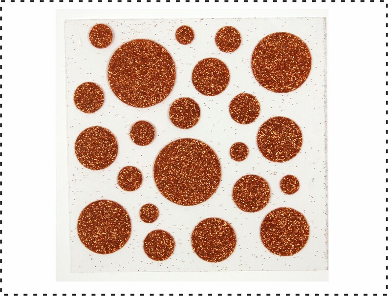 Op de afbeelding: Een vel wit papier met 20 koperkleurige glittercirkels in verschillende maten. De cirkels zijn in een willekeurig patroon gerangschikt.